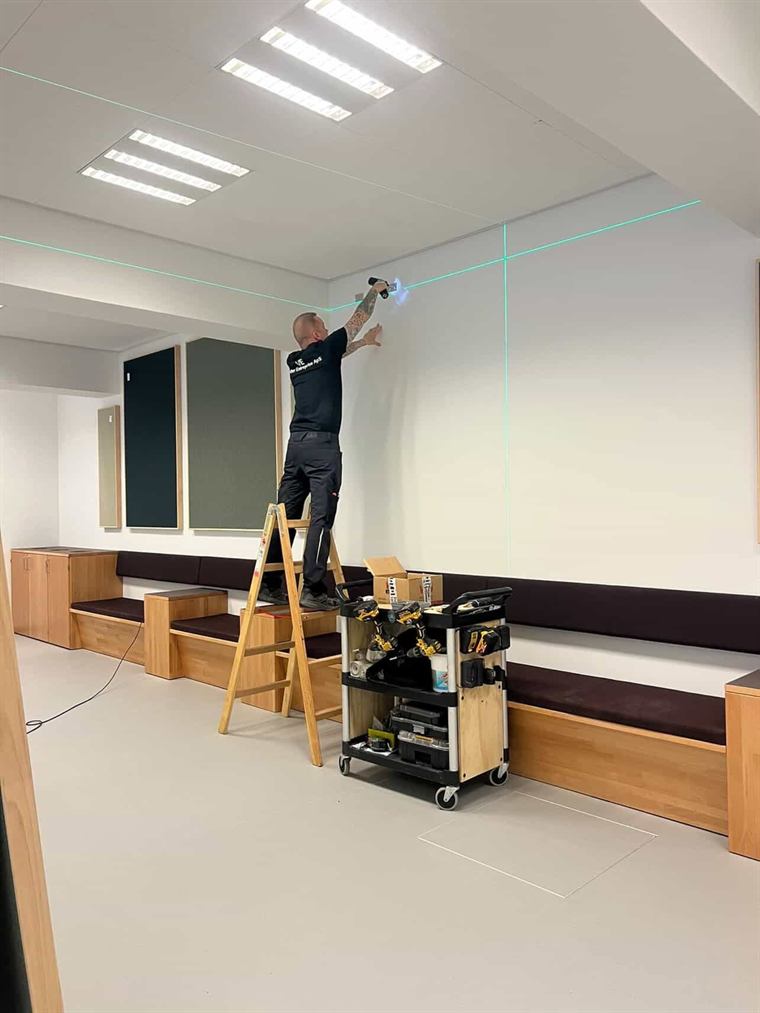 Håndværker på stige arbejder efter en laserlinje i et rum med indbyggede bænke